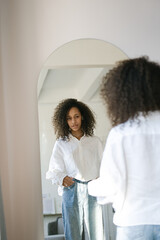 Cute african american girl choosing clothes to wear in front of mirror in i the living room. Morning wake up concept       