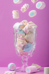 Multicolored marshmallows in a glass over pink background