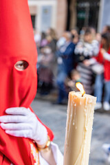 The candle in flame of a young Nazarene with a red hood doing his penance station in the Holy Week...