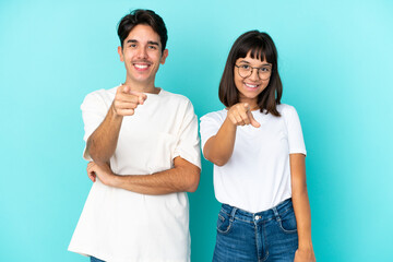 Young mixed race couple isolated on blue background points finger at you with a confident expression