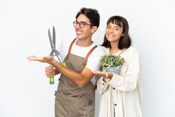 Young mixed race gardeners holding a plant and pruning shears isolated on white background pointing...