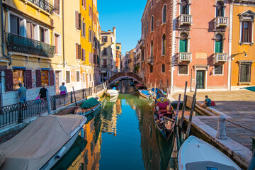 View of empty gondola on narrow canals, with a tourist waiting for the gondolier of Venice, Italy. - obrazy, fototapety, plakaty