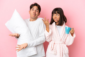 Young couple in pajamas isolated on pink background making doubts gesture while lifting the shoulders