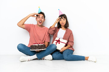 Young mixed race couple celebrating a birthday sitting on the floor isolated on white background has just realized something and has intending the solution