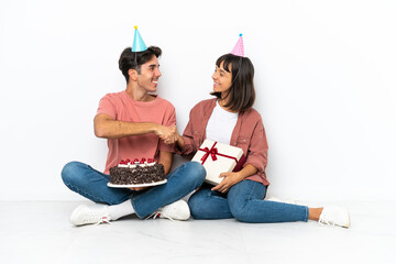 Young mixed race couple celebrating a birthday sitting on the floor isolated on white background handshaking after good deal