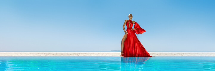 Luxury fashion. Elegant fashion model. Stylish female model in red long gown dress on the Maldives beach. Elegance. Classy woman in amazing red dress near the pool. Couture. Vogue. Panorama.