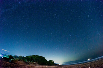魚眼レンズで撮影した夜の海岸と星空