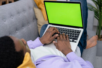 Black man using laptop notebook viewing green screen press keyboard browsing chroma key, African American freelancer online typing text working remotely on computer close up from home.