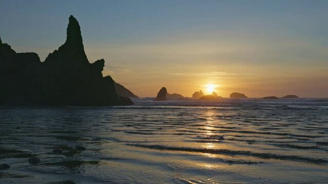 Sunset on huge sandy ocean beach among bizarre stones and rocks. Near Coos Bay, Bandon, Oregon, United States. Gimbal high quality shot, 4K