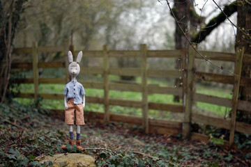 Сute doll bunny in a  plaid shirt standing in front of the wooden fence