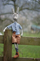Funny doll bunny in a  plaid shirt standing on a wooden fence