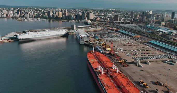 Aerial panning view of two Autoliner ships delivering vehicles docked at Durban harbour, Durban city centre in background
