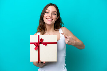 Young caucasian woman holding a gift isolated on blue background with surprise facial expression