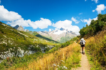 Senior man hiking French Alps in summer with solar backpack. The Aiguille des Glaciers, mountain in the Mont Blanc massif. View From Chapieux valley, Savoie, France. - obrazy, fototapety, plakaty