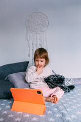 Naklejka premium Small child watches cartoons at home on sofa on the tablet. Kid use technology