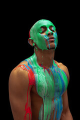 Portrait of young bald man covered with multicolored paint flowing down his body isolated over black background