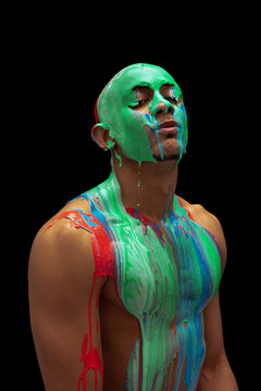 Portrait of young bald man covered with multicolored paint flowing down his body isolated over black background