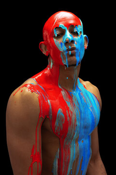 Portrait of young man being covered with blue and yellow thick paint flowing down his head on shoulders and body isolated over black background