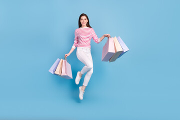 Full size photo of cheerful pretty lady shopper hold packages jumping isolated on blue color...