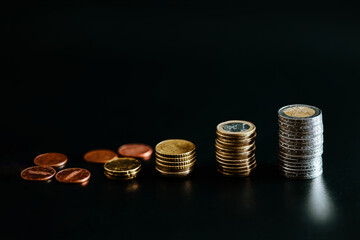 Euro coins stacked on each other with several pile of smaller coins on table isolated on black...