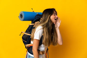 Young mountaineer woman with a big backpack isolated on yellow background shouting with mouth wide open to the side