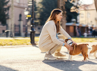 A woman in a park crouching and petting a dog.
