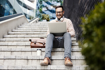 Fototapeta premium A happy man sits on the stairs outside and using laptop.