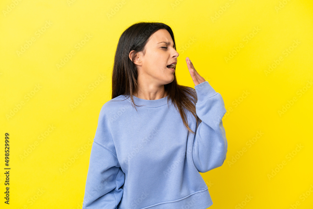 Wall mural Young caucasian woman isolated on yellow background yawning and covering wide open mouth with hand