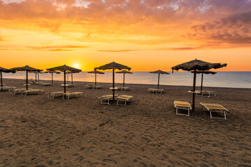  empty beach during beautiful sunrise or sunset with chaise loungues and nice umbrellas with blue sea