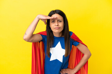 Woman isolated on yellow background in superhero costume and showing something