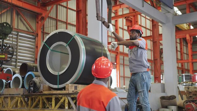 African industrial workers work together using hooks from electric hoists. Let the hand symbol lower the level of the hook.