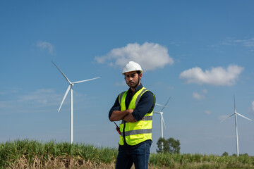 engineer with wind turbine. Young man maintenance engineer  working with tablet and radio communication in wind turbine farm on blue sky background.
