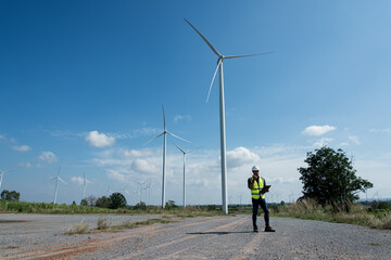 engineer with wind turbine. Young man maintenance engineer  working with tablet and radio communication in wind turbine farm on blue sky background.