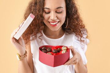 Beautiful young woman with delicious chocolate candies in box on color background