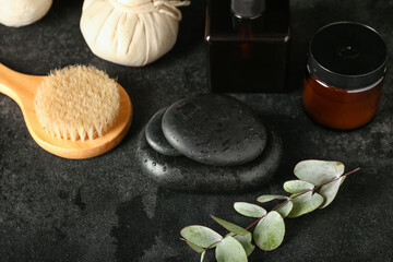Wet spa stones with cosmetics and massage brush on dark background