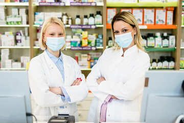Two blond female pharmacists with protective mask on their faces working at pharmacy. Medical healthcare concept.