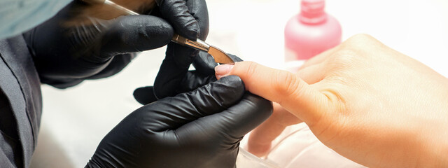 Close up professional manicurist master holding customer hand while using a cuticle pusher in a nail salon - obrazy, fototapety, plakaty