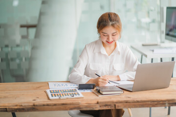 Portraits of beautiful smiling Asian women relax using laptop computer technology while sitting on their desks and using their creativity to work, work from home concept.