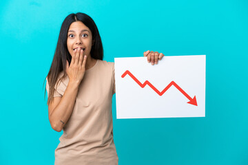 Young woman over isolated background holding a sign with a decreasing statistics arrow symbol with surprised expression