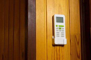 Air conditioner remote control in a holder on the wall. Home climate control. Energy saving. Remote control off.