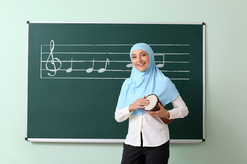 Muslim music teacher with drum near blackboard in classroom