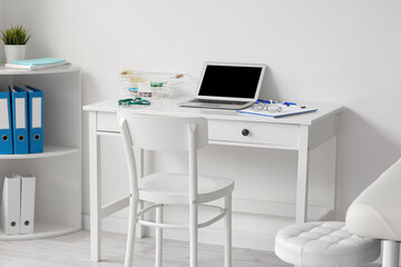 Doctor's workplace with laptop near white wall in medical office