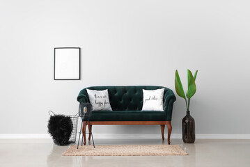 Vase with palm leaves, green sofa, lamp and basket near light wall