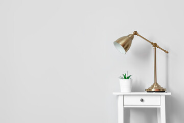Modern lamp and flowerpot on table near light wall