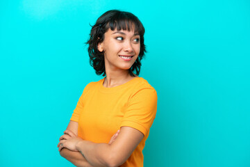 Young Argentinian woman isolated on blue background with arms crossed and happy