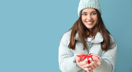 Young woman in warm gloves with gift box on blue background