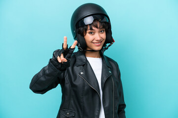 Young Argentinian woman with a motorcycle helmet isolated on blue background smiling and showing victory sign