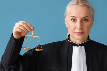 Mature female judge in robe with justice scales on blue background