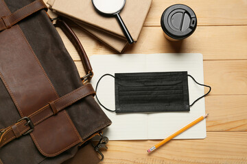 Bag, notebooks, magnifier, paper cup of coffee and medical mask on wooden background