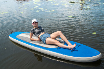 pretty young slim female model lying on sup board at sunny morning at ocean beach